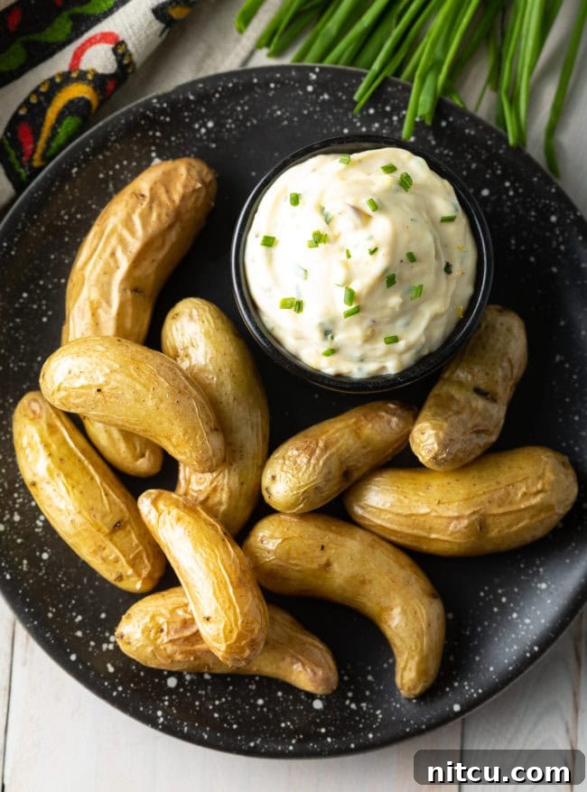 easy aioli sauce in a black bowl on a black plate with fingerling potatoes.
