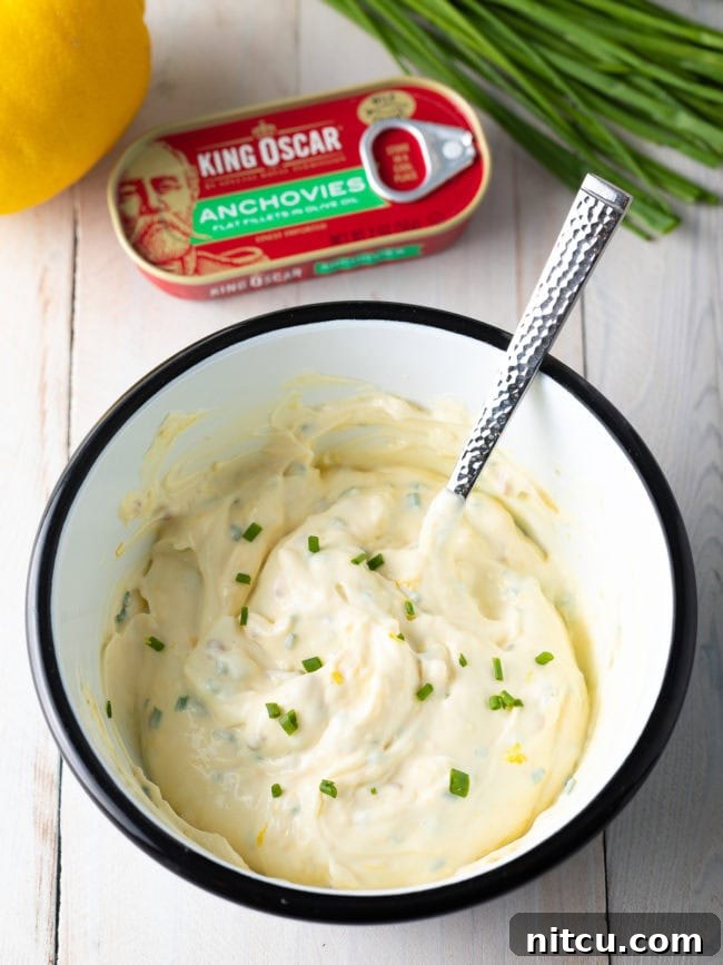 A white bowl with ingredients for aioli sauce with a spoon that has stirred the mixture.
