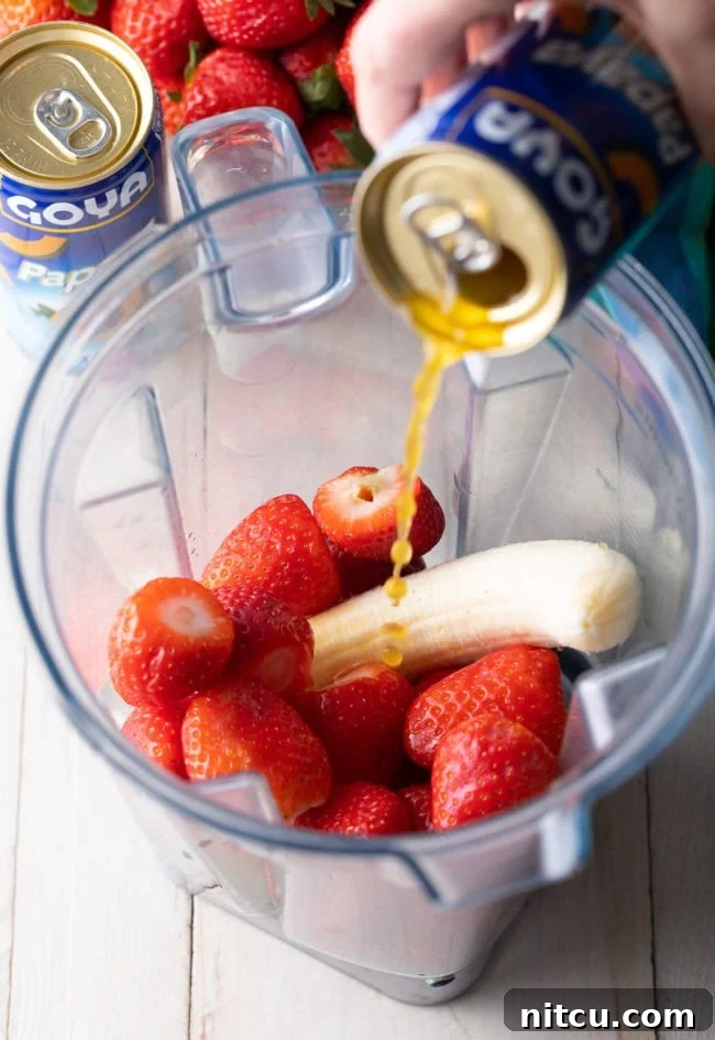 Strawberries and banana in a blender with papaya nectar being poured in. 