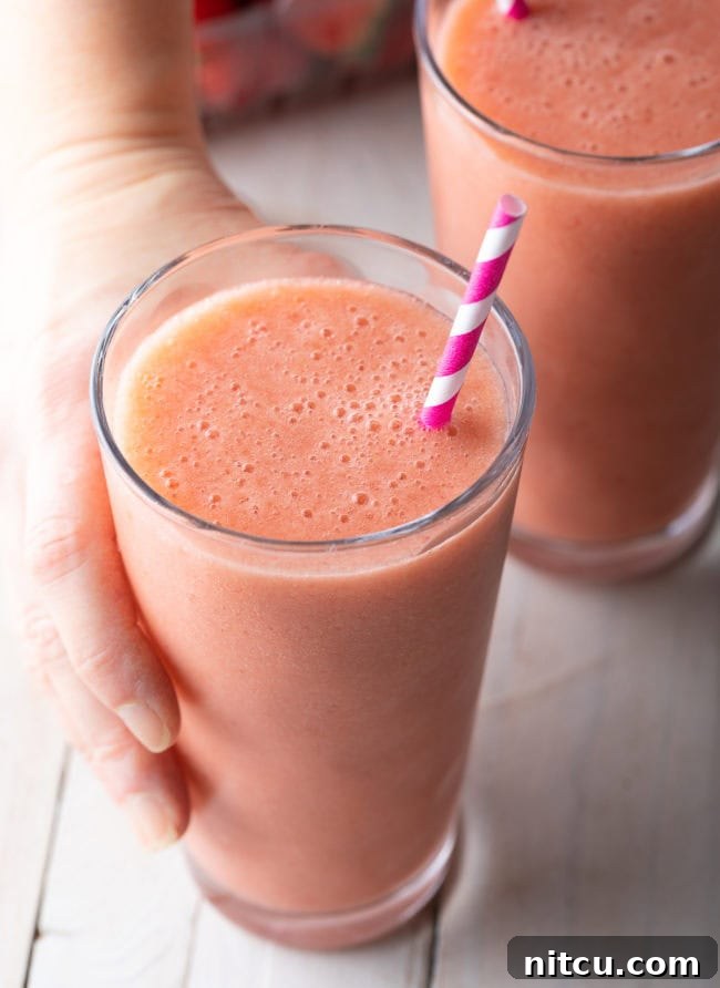 Hand holding a strawberry banana smoothie with a straw in it. 