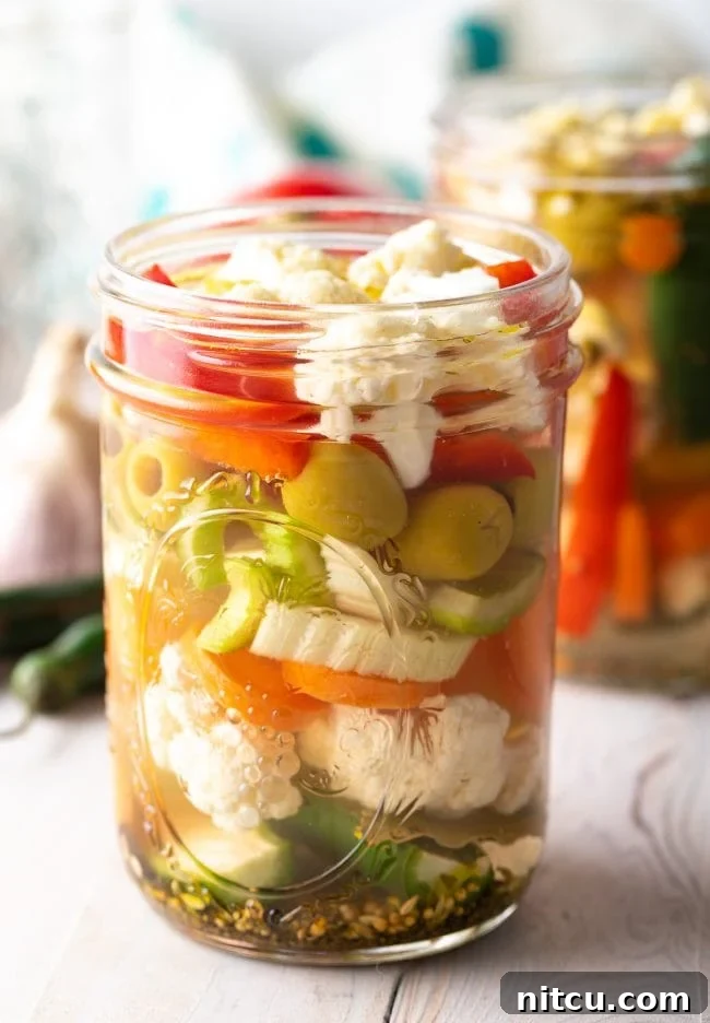 Two jars of homemade Giardiniera pickled vegetables, with fresh vegetables blurred in the background, highlighting the ready-to-eat product.