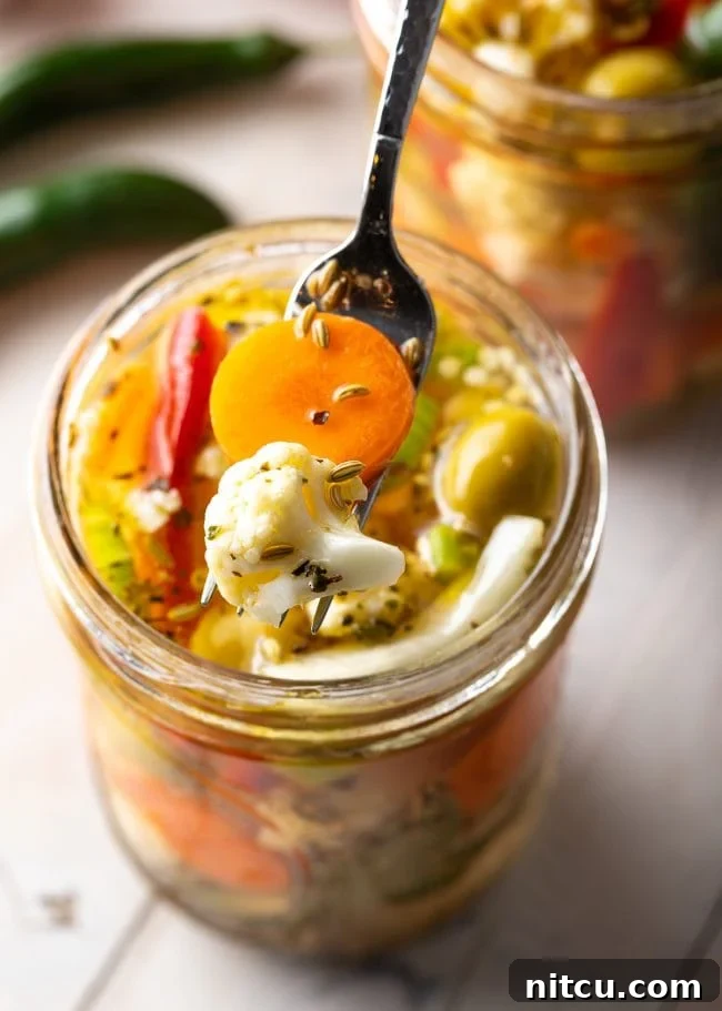 A fork lifting some colorful giardiniera pickled vegetables from a glass jar, showing the crisp texture.