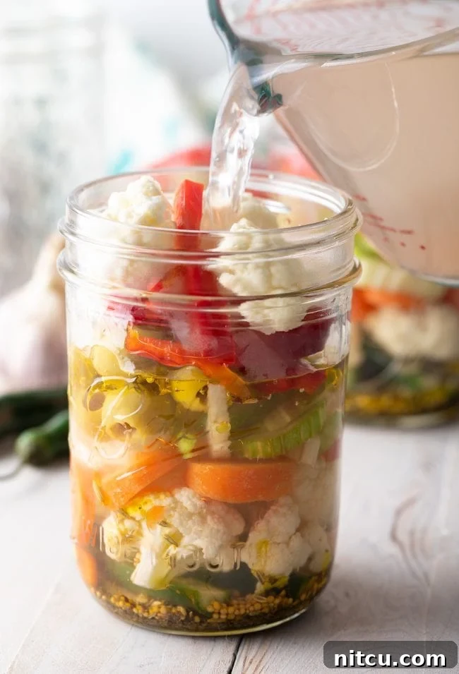 Freshly boiled pickling brine being carefully poured over the packed vegetables and spices in a jar.