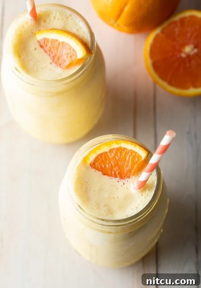 Overhead shot of two jars filled with orange Julius smoothies, garnished with fresh orange slices and straws.