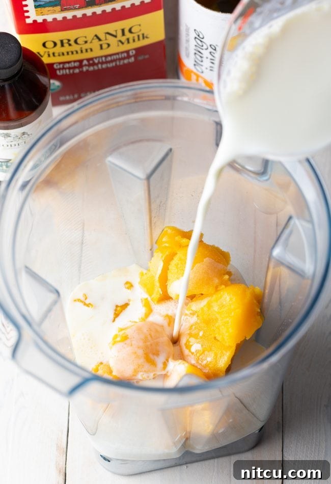 Pouring milk into a blender containing frozen orange juice concentrate.