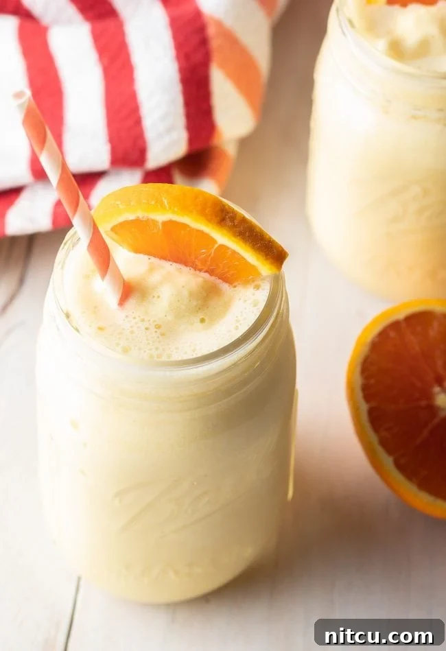 A glass jar filled with Orange Julius, topped with a slice of fresh orange.