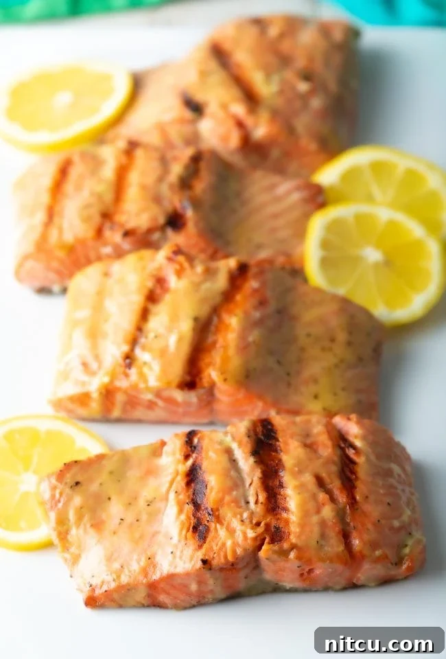 Grilled salmon fillets on white platter, garnished with fresh herbs.