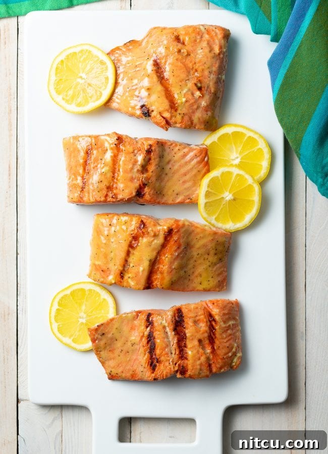 Top down view of grilled salmon on a platter with slices of lemon and fresh pineapple.