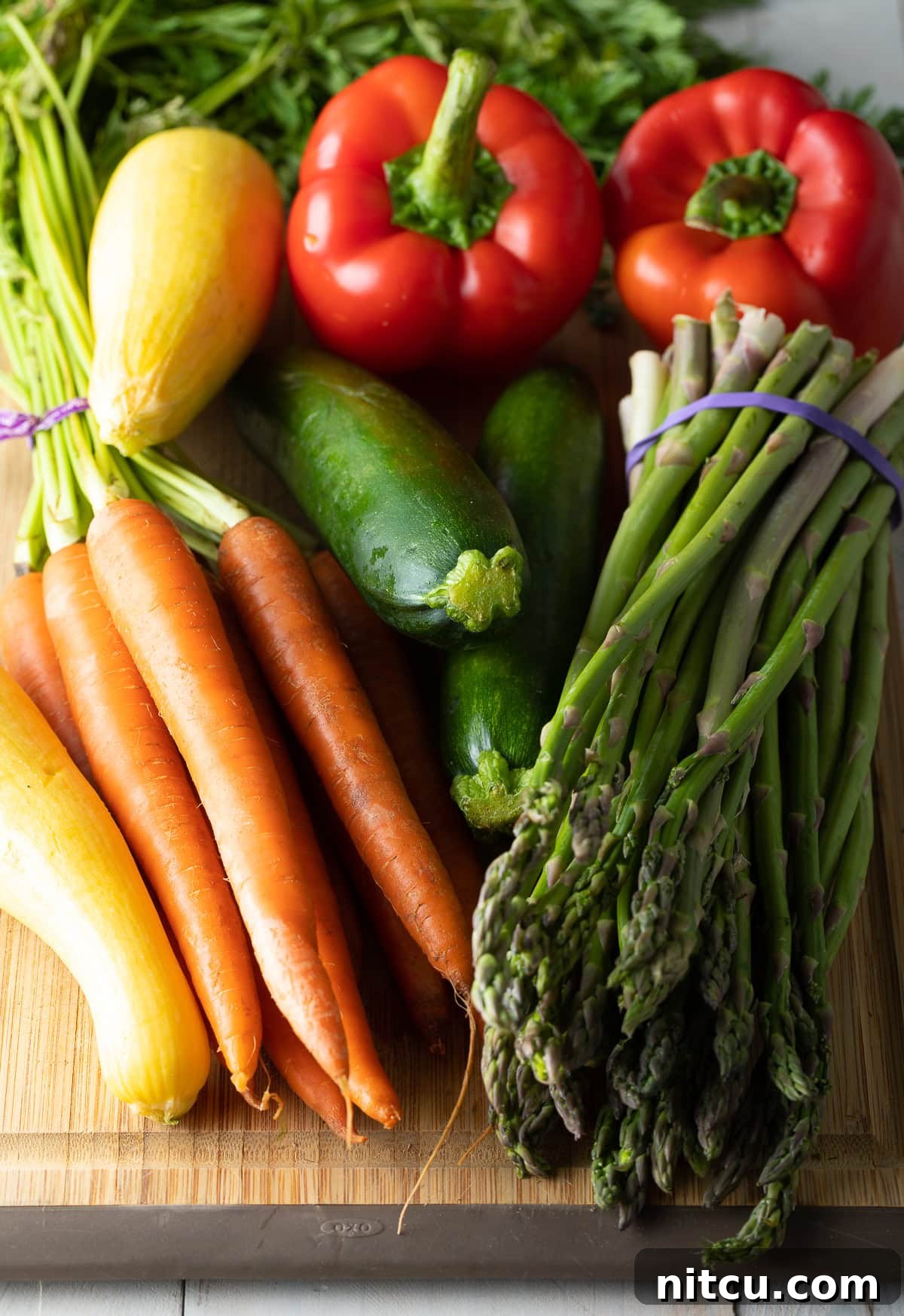 An assortment of fresh, raw vegetables ready for grilling, including carrots, asparagus, zucchini, and bell peppers.