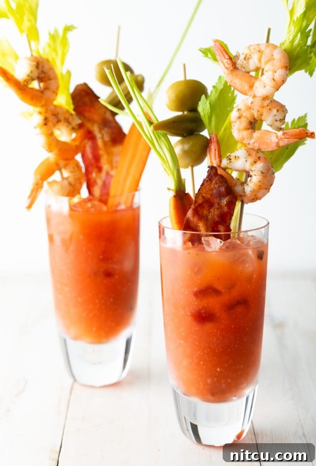 Closeup view of 2 Bloody Mary cocktails garnished with shrimp, bacon, celery, olives and carrots. 