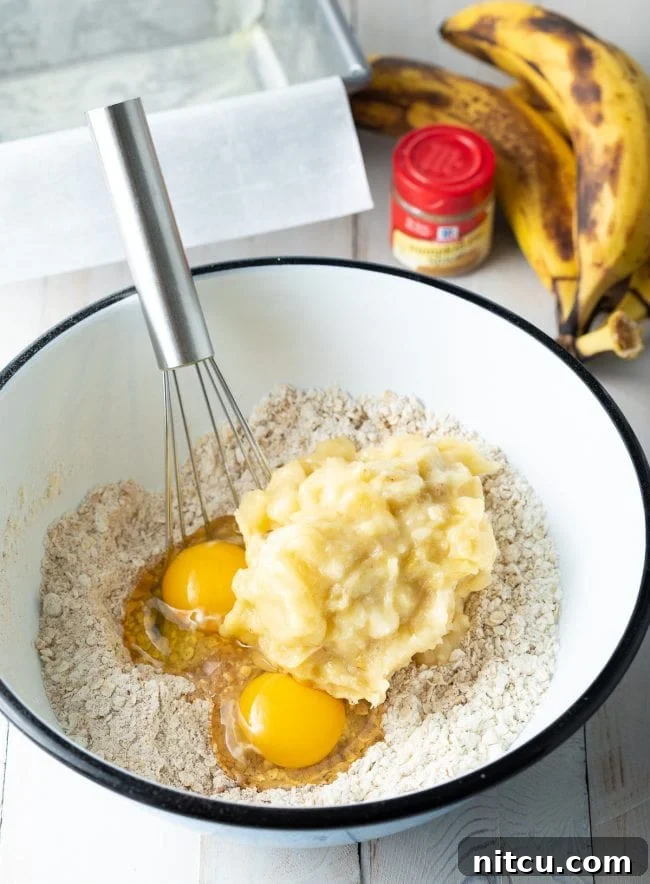 Flour and oats with mashed banana and eggs in a mixing bowl.