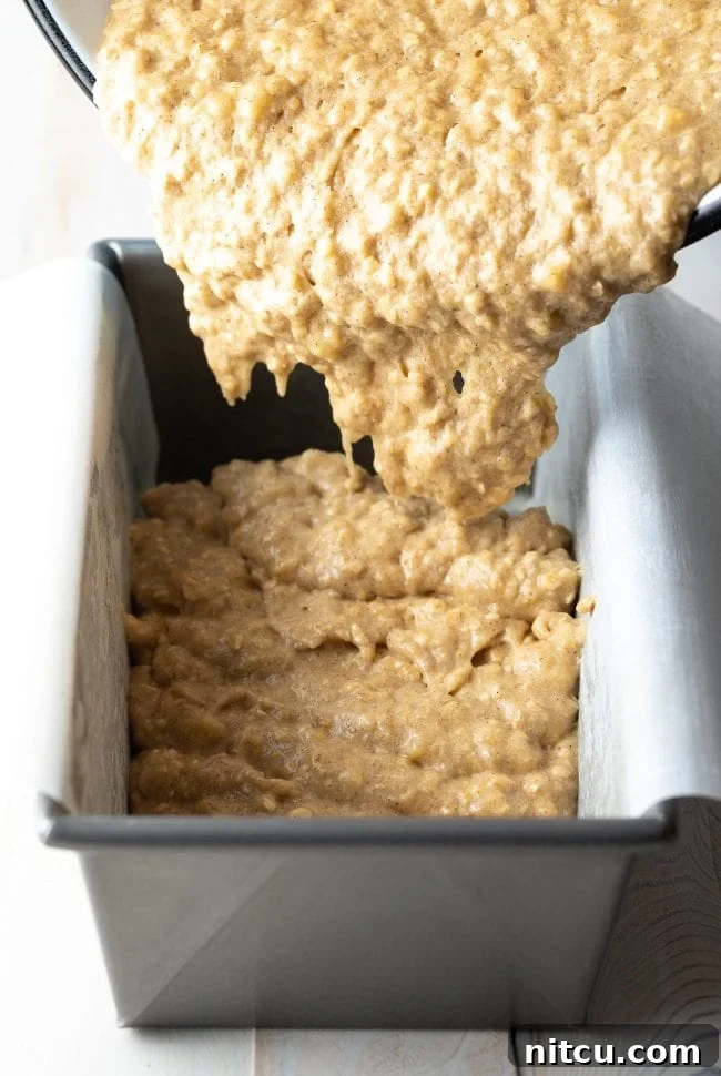 Banana bread batter being transferred into a baking dish lined with parchment paper for easy removal.
