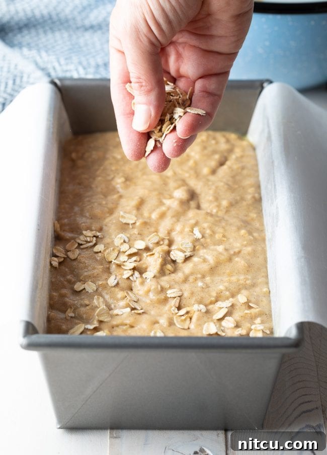 A hand gently sprinkling extra oats onto the top of banana bread batter before baking.