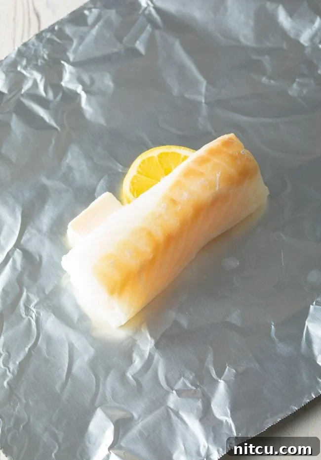 White fish fillets seasoned with lemon pepper and butter, wrapped in aluminum foil ready for grilling.