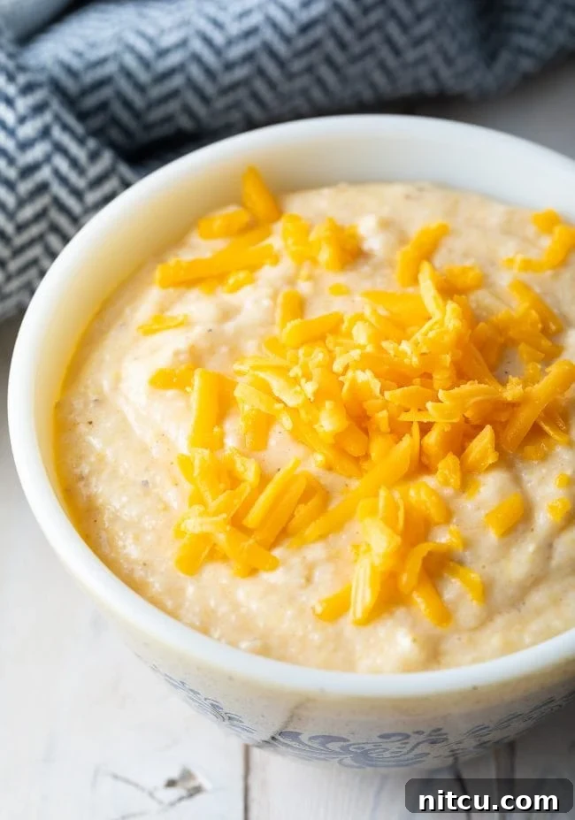 Creamy Cheese grits recipe in a white bowl with shredded cheddar cheese on top. 