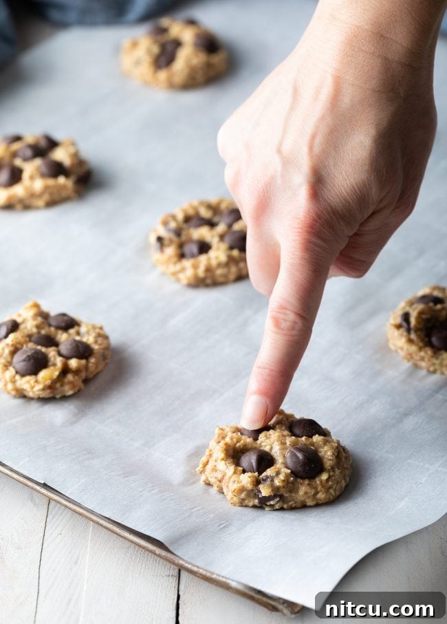 Hand pointing to a chocolate chip in a banana oat cookie on parchment paper.