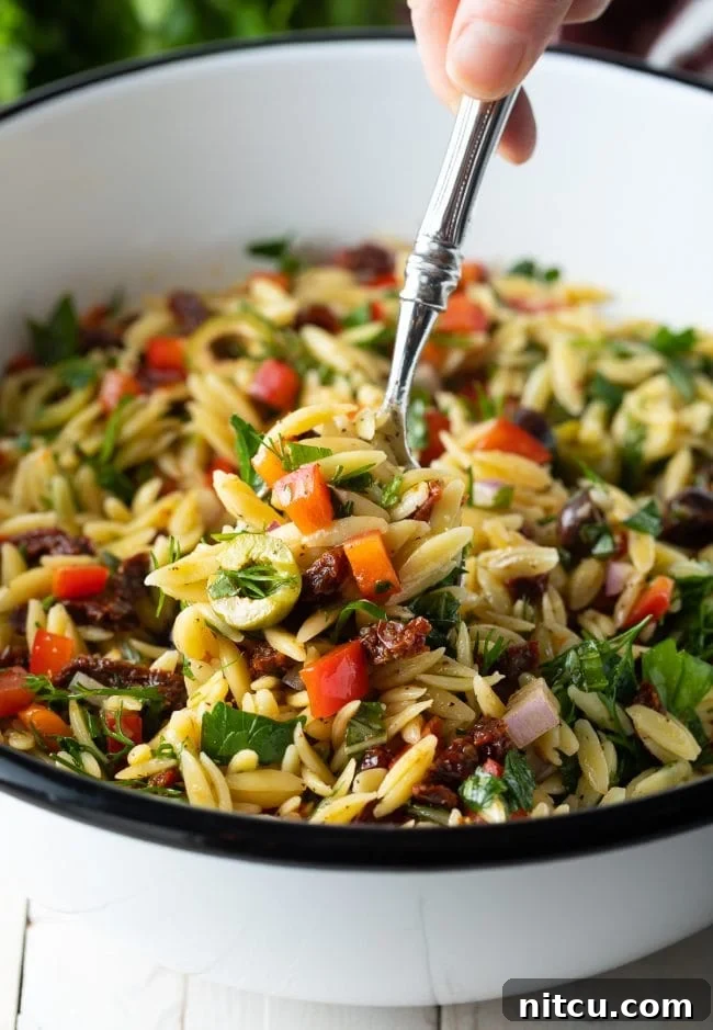 Close-up of a spoon scooping up a portion of Mediterranean Orzo Salad with lemon vinaigrette from a white bowl.