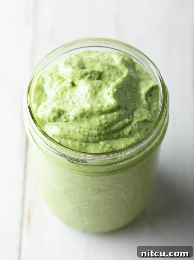 A close-up shot of a jar filled with luscious, vibrant green creamy pesto sauce, ready to be enjoyed.