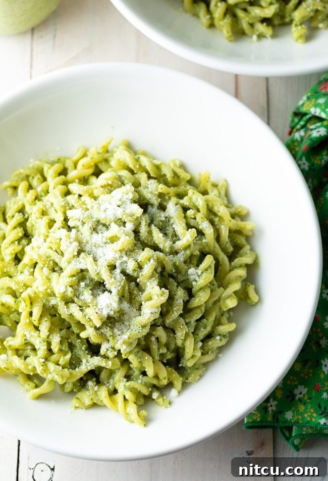 Delicious fusilli pasta generously coated in creamy pesto sauce, garnished with grated Parmesan cheese, served in an elegant white bowl.