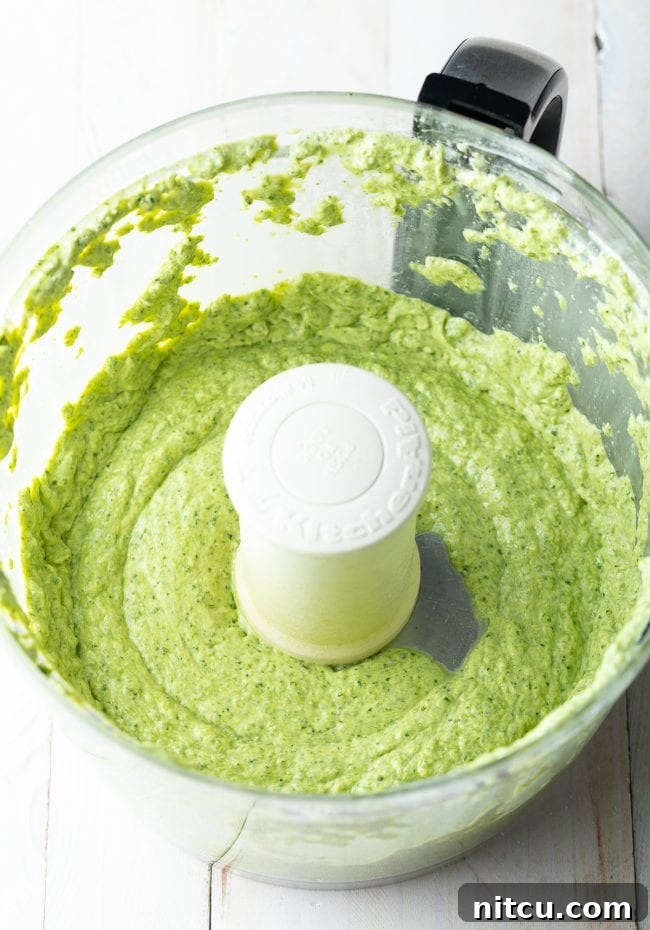 Smooth, vibrant green creamy pesto sauce in a food processor bowl after being thoroughly mixed.