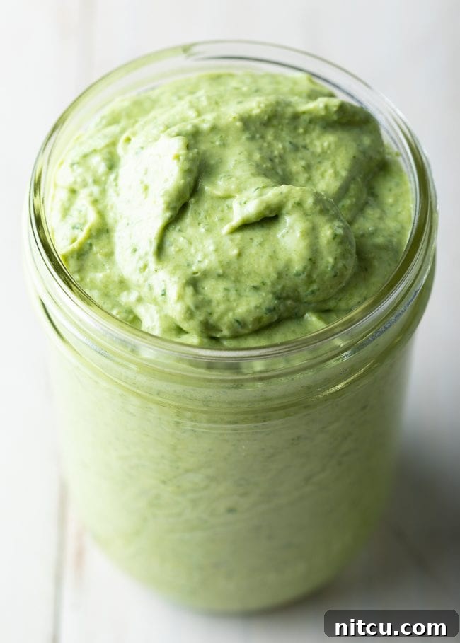 A charming glass jar filled with luscious, homemade creamy pesto, sitting on a rustic wooden surface, ready to be served.