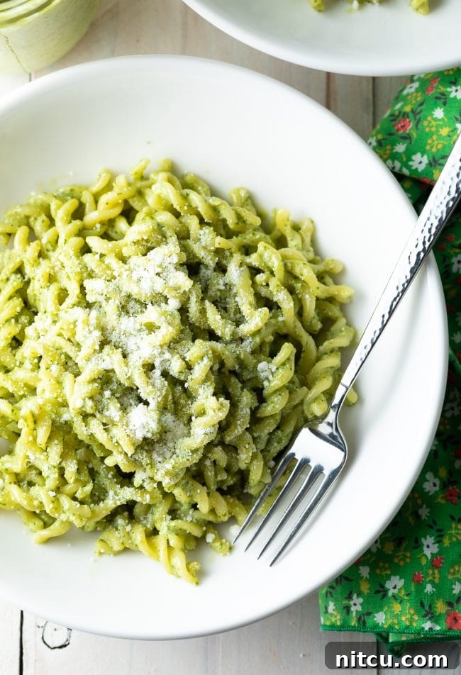 An inviting overhead view of pesto pasta in a white bowl, adorned with fresh basil, accompanied by a fork resting beside it.