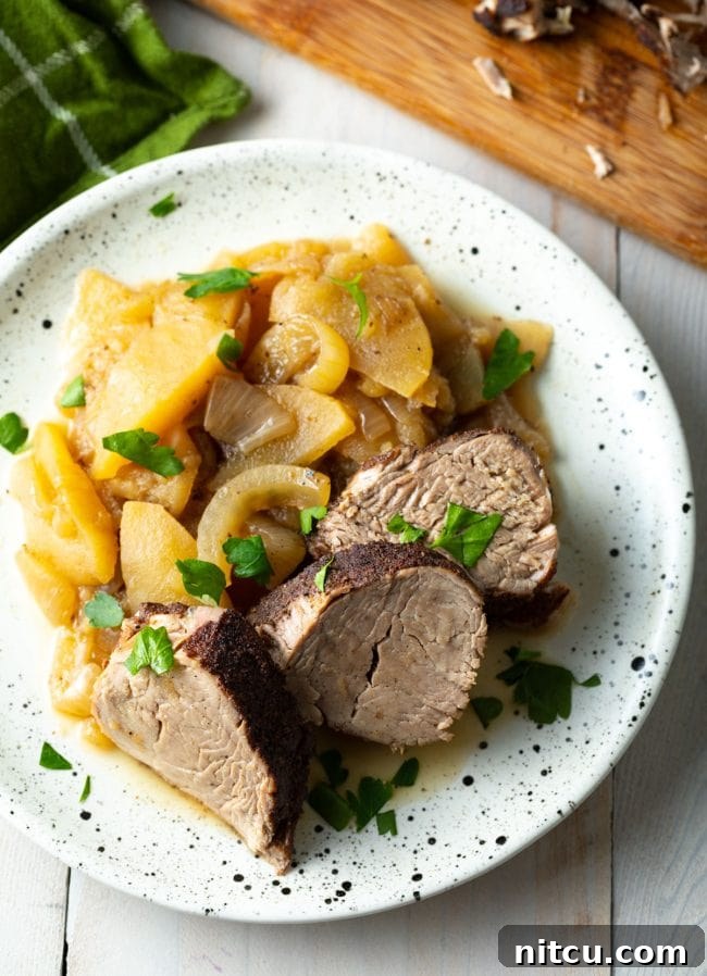 Overhead shot of pork tenderloin slices with apples and onions on a white speckled plate.