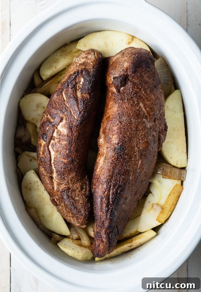 Spice rubbed pork in the crock pot on a bed of apples and onions.