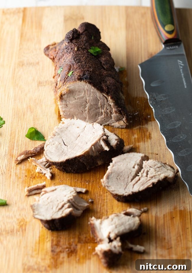 Pork tenderloin on a cutting board being sliced with a sharp knife.