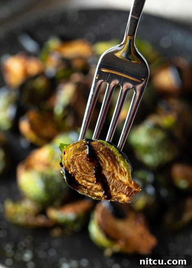 Crispy Brussels sprout recipe with balsamic picked up with fork, close-up.
