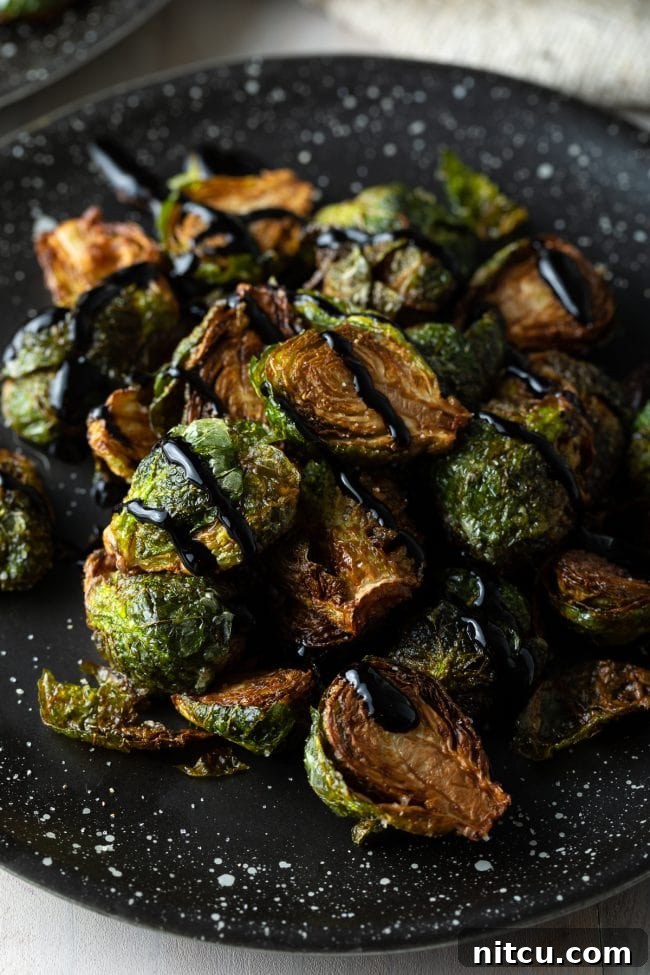 Fried Brussel sprouts with balsamic glaze in black speckled plate, ready to serve.