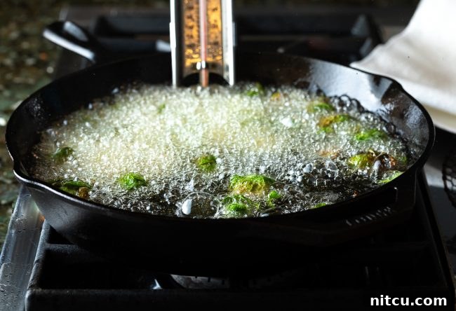 Fried Brussels sprouts cooking in hot oil in a skillet, capturing the frying process.