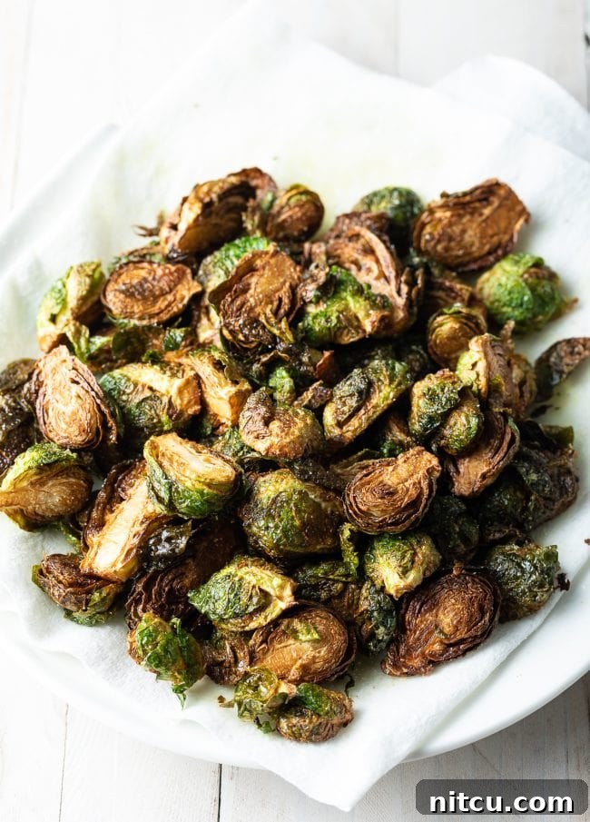 Fried Brussels sprouts being strained on kitchen paper on a plate, removing excess oil.