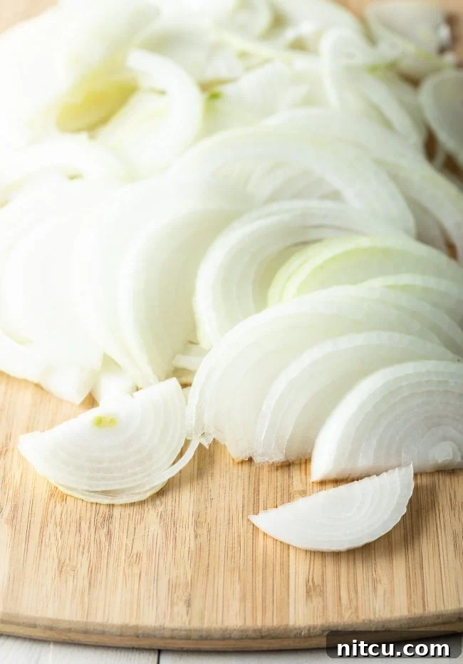 Sliced white onions on a wooden cutting board, ready to be prepared for the crispy topping.