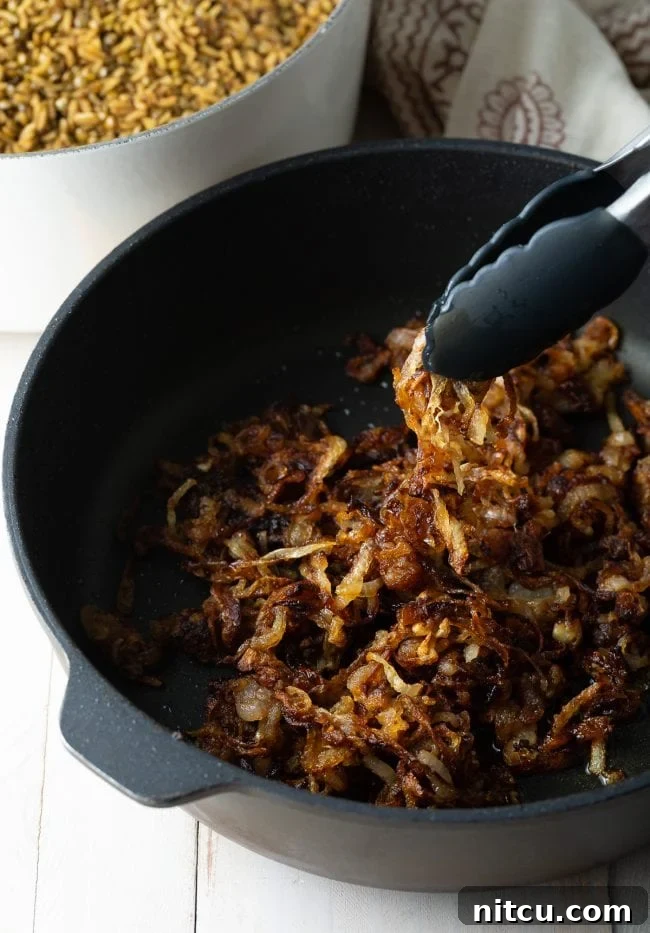 Crispy fried onions being carefully removed from a skillet with tongs, perfectly golden brown.