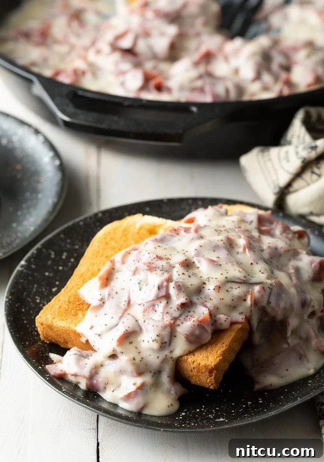 Creamed chipped beef on toast served on a black plate, garnished with fresh parsley.