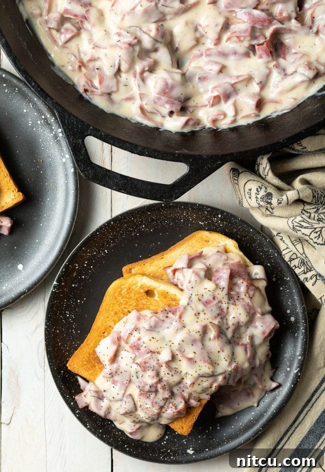 Two slices of golden toast lavishly topped with creamy chipped beef gravy on a black plate.