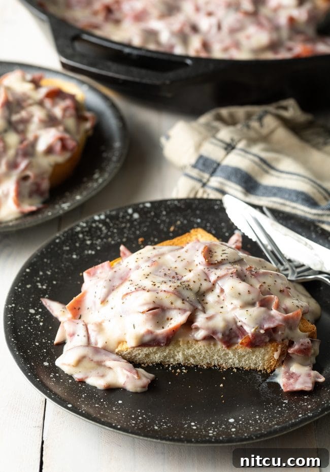 Creamed chipped beef on top of toast, cut in half, showcasing its rich texture on a black plate.
