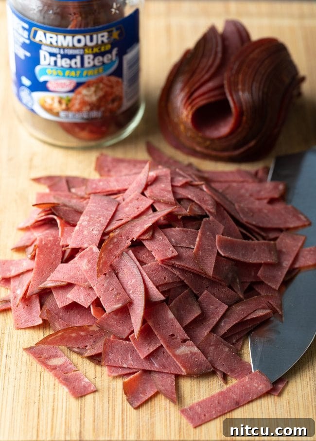 Thin strips of Buddig dried beef laid out on a wooden cutting board, ready for preparation.