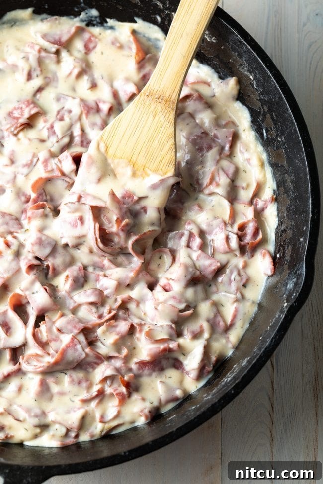 Rich, homemade chipped beef gravy simmering in a cast iron skillet, stirred with a wooden spoon.