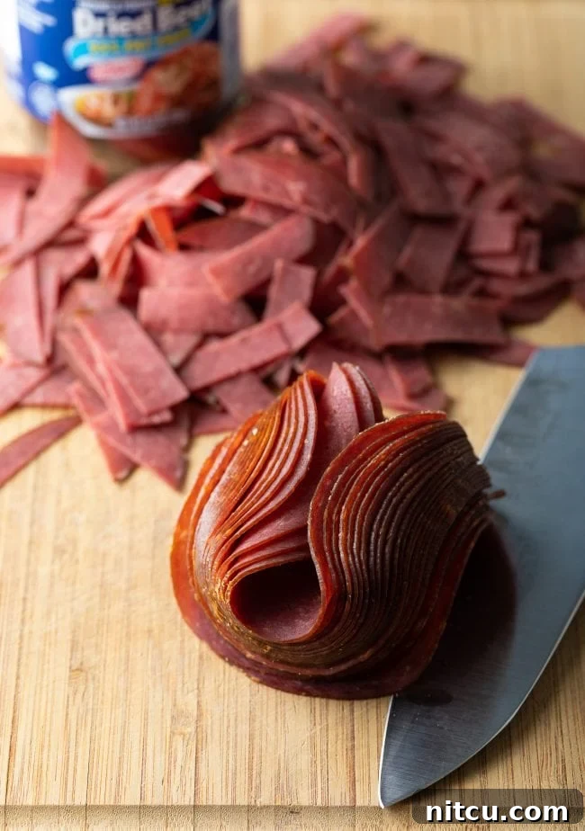 Folded slices of Buddig Beef arranged on a wooden surface, with a knife nearby for preparation.