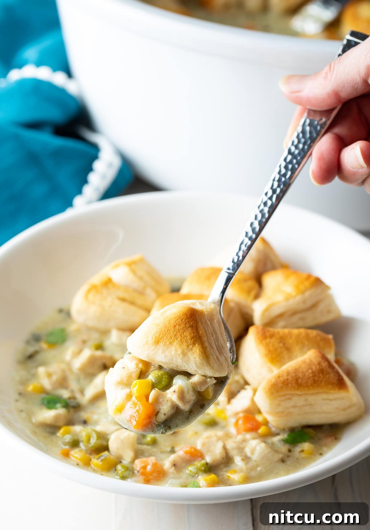 Hand holding a spoon with a bite of chicken pot pie mixture and biscuit.