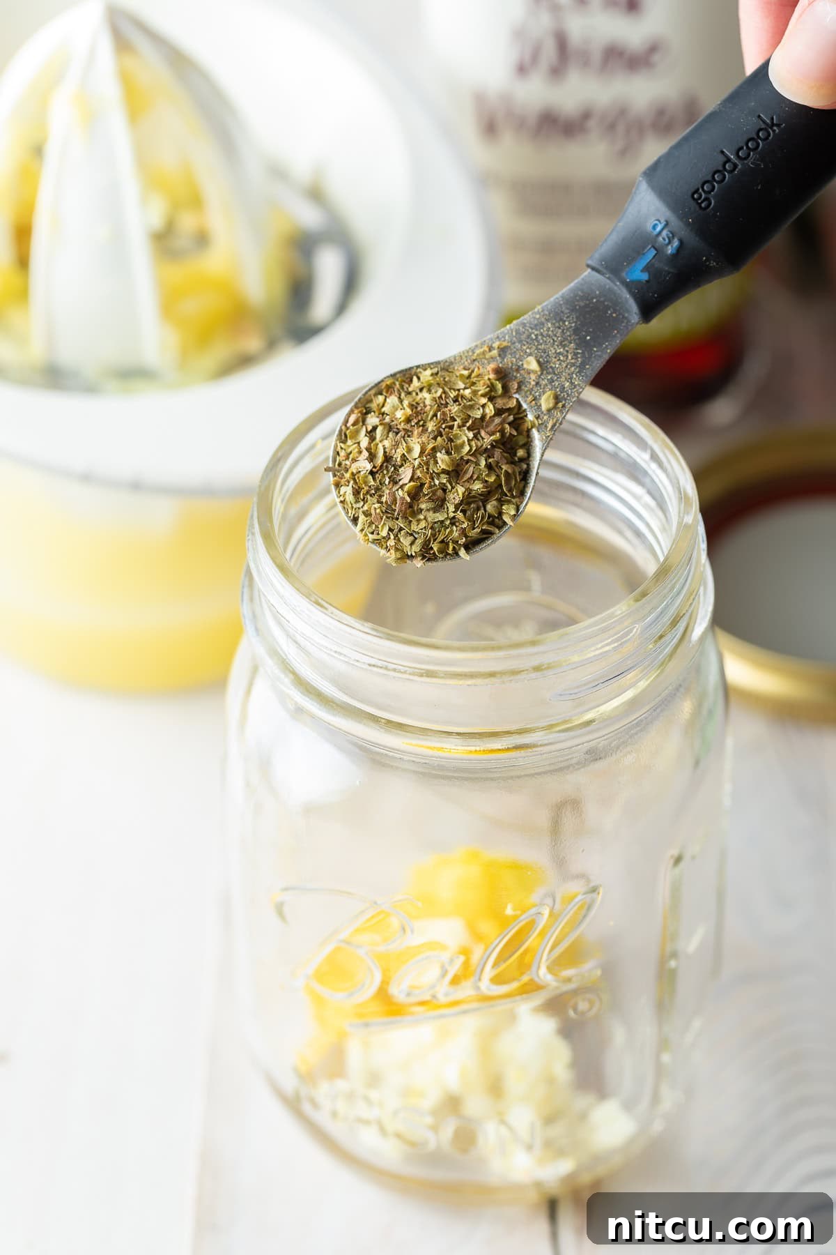 A teaspoon holding Greek seasoning over a glass jar, ready to be added to the dressing.