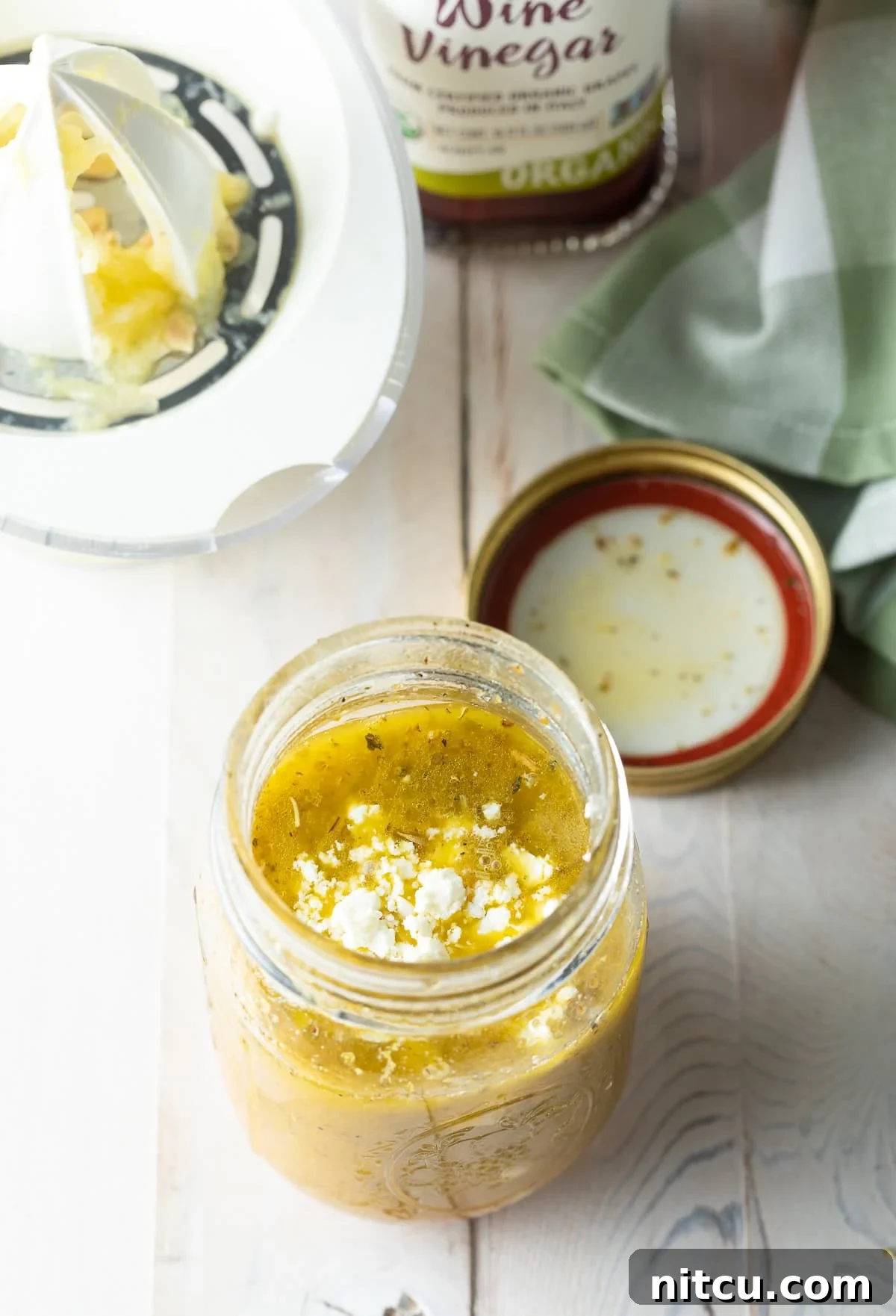 A close-up of a hand pouring red wine vinegar into a jar, a key ingredient for tang.