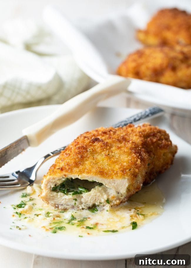 Golden brown pan-fried Chicken Kiev, expertly cut open to reveal its luscious, melting garlic butter filling, elegantly served on a plate with a fork poised for a bite.