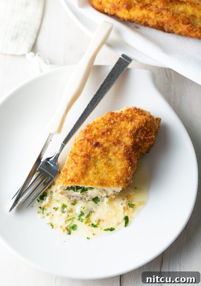 A mesmerizing close-up of a pan-fried Chicken Kiev, elegantly sliced open to prominently display the luscious, melted garlic butter gently oozing out onto a pristine white plate, promising an exquisite culinary experience.