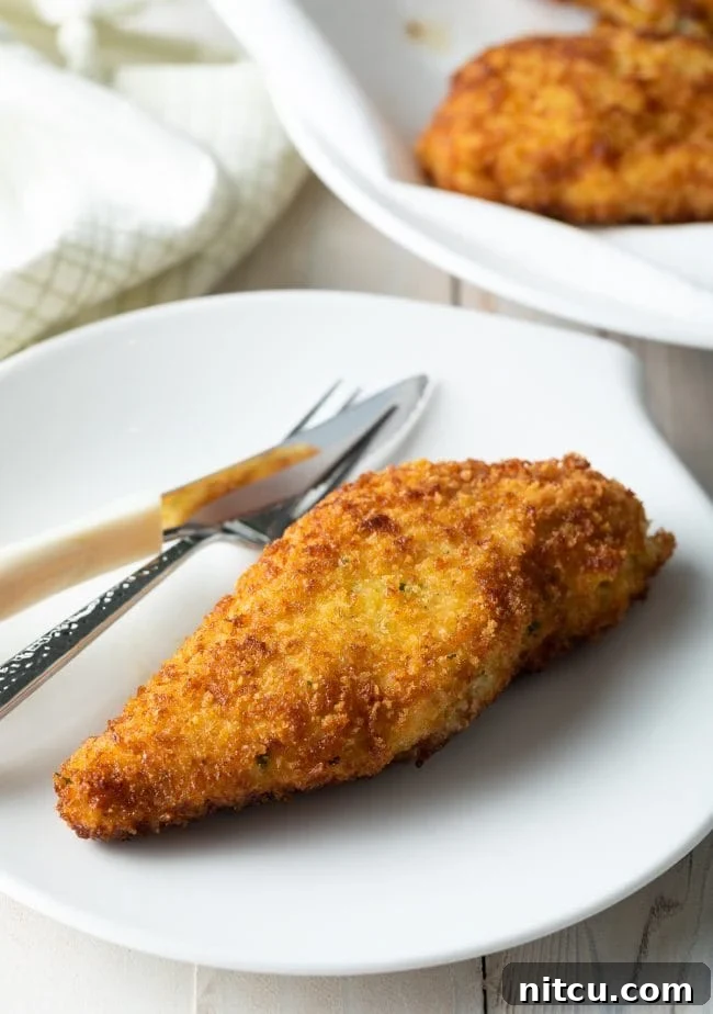 A perfectly cooked, simplified pan-fried Chicken Kiev presented with a fork and knife on a crisp white plate, elegantly showcasing its golden crust and inviting texture, ready to be savored.