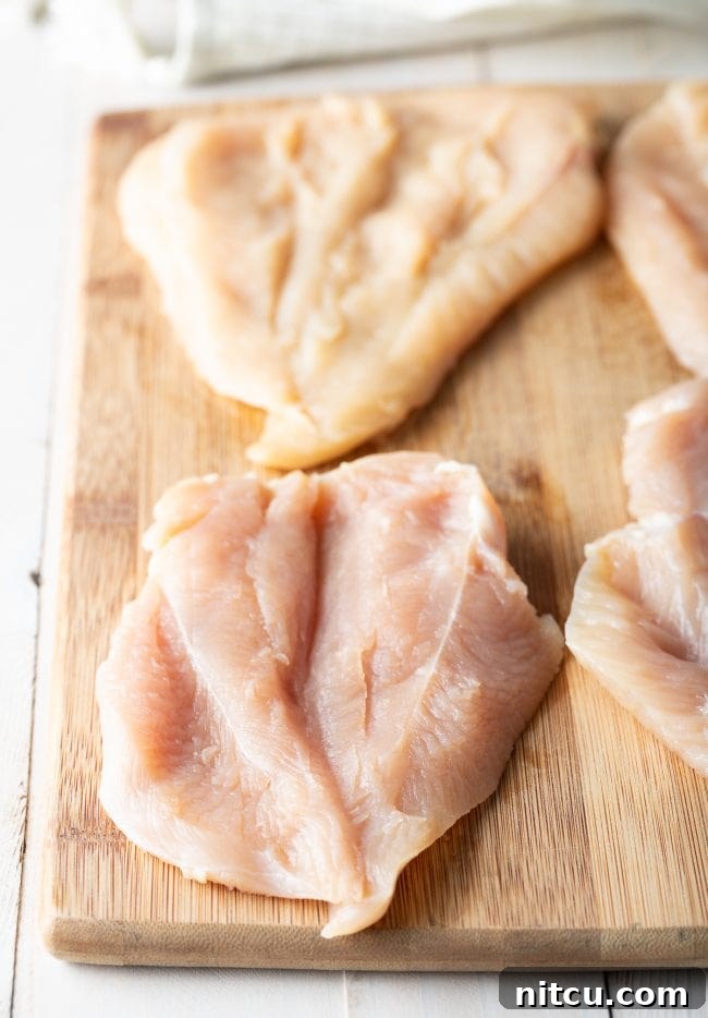 Raw chicken breasts, precisely butterflied and laid flat on a rustic wooden cutting board, meticulously prepared and ready for the stuffing process.