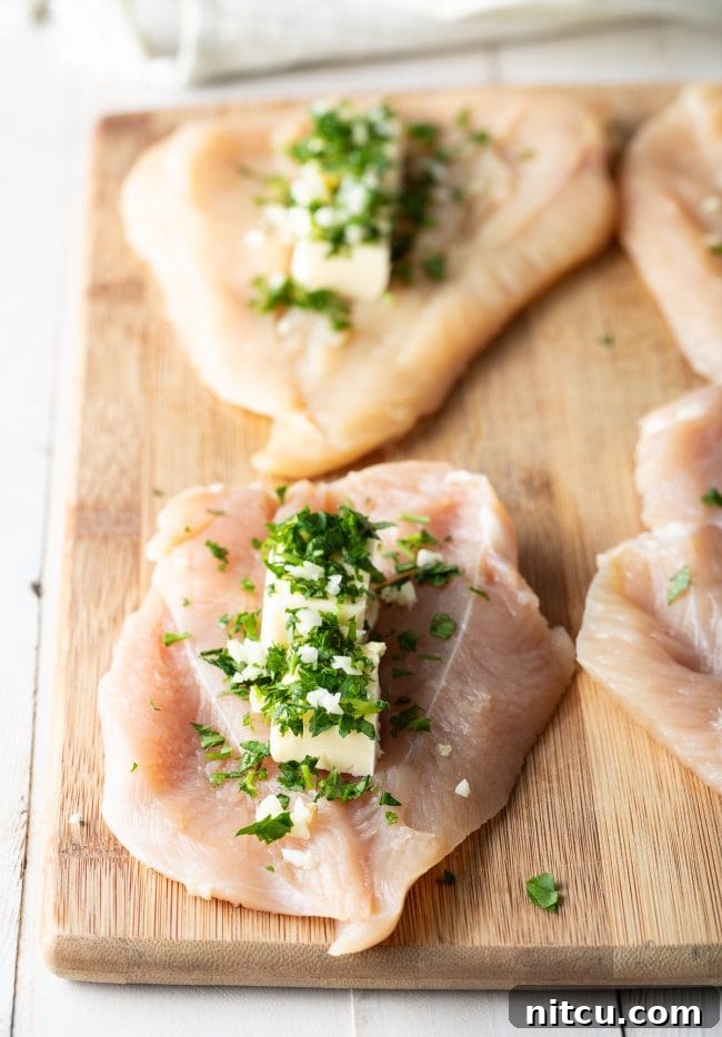 Butterflied chicken breasts with carefully placed mounds of creamy, herb-infused garlic butter filling situated in the center on a wooden cutting board.