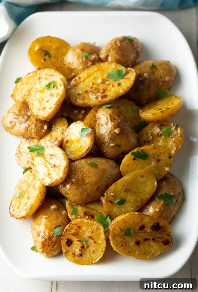 Baby greek potatoes with lemon, garlic, and parsley resting on a white platter.